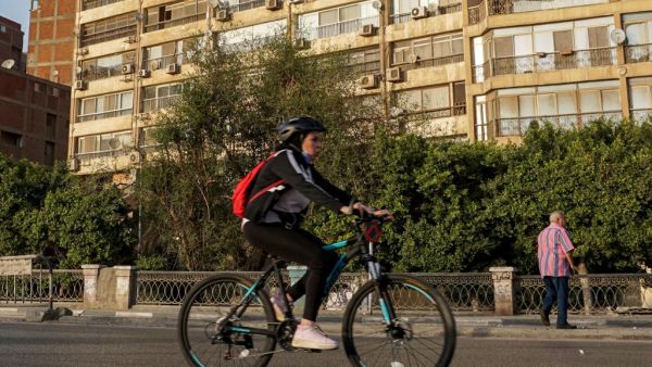 A woman cycles while wearing a face mask around her neck along the Nile riverfront in the Egyptian capital Cairo's southern district of Maadi on May 22, 2020, during the COVID-19 coronavirus pandemic. Khaled DESOUKI / AFP