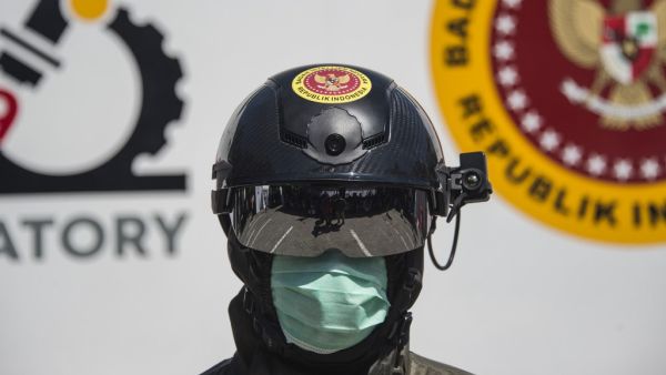 An official from Indonesia's state intelligence agency wears a helmet equipped to measure the body temperature of people at the venue of a rapid test for the COVID-19 coronavirus in Surabaya on June 4, 2020. Juni Kriswanto / AFP
