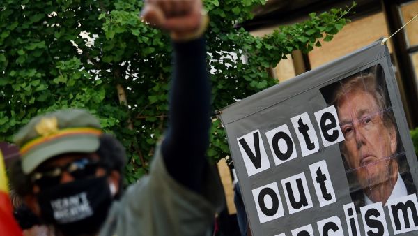 A demonstrator raises his fist in front of a sign calling to vote out racism with a picture of President Donald Trump during a peaceful protest against police brutality and the death of George Floyd, on June 7, 2020 in Washington, DC. Olivier DOULIERY / AFP