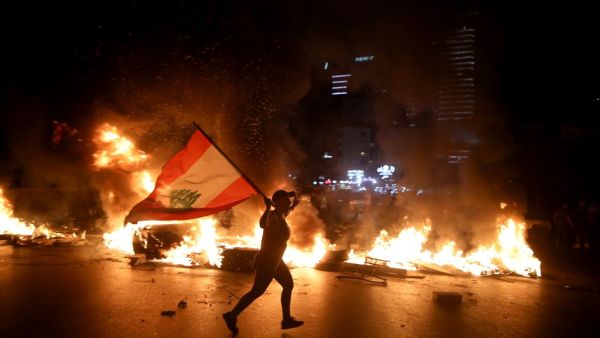 A protester holding the Lebanese flag runs as protesters block the Jounieh Tripoli highway with flaming tires set aflame during a demonstration against dire economic conditions in Jal el Dib North East of the Lebanese capital Beirut late on June 11, 2020. Patrick BAZ / AFP