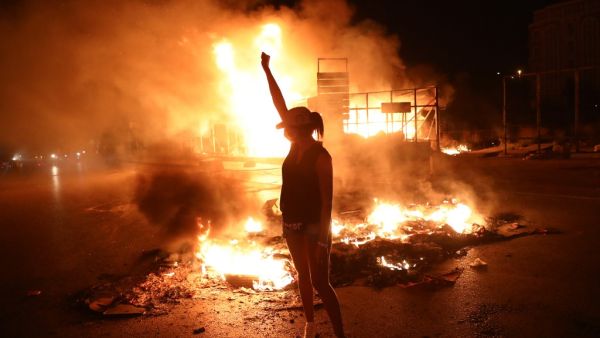 A Lebanese anti-government protester raises her clenched fist as tires burn behind her during a demonstration against dire economic conditions in the downtown districtof the capital Beirut, late on June 11, 2020. The Lebanese pound sank to a record low on the black market on June 11 despite the authorities' attempts to halt the plunge of the crisis-hit country's currency, money changers said. Lebanon is in the grips of its worst economic turmoil in decades, and holding talks with the International Monetary 