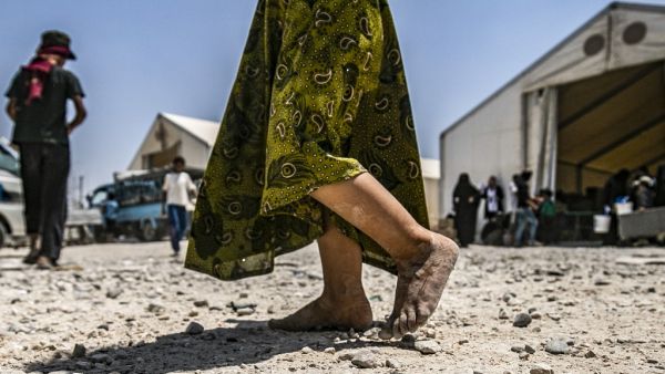 In this file photograph taken on July 22, 2019, a young child walks barefoot at al-Hol camp for displaced people, in al-Hasakeh governorate, north-eastern Syria, as people collect UN-provided humanitarian aid packages. The government said June 22, 2020, that it had brought home 10 French children of jihadist fighters overnight from a refugee camp in Syria, the latest in a piecemeal repatriation process since the Islamic State group was ousted from its Syrian base in March 2019. Delil souleiman / AFP