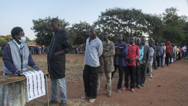 An electoral official (L) checks the voters' roll while people queue to vote at the Malembo polling station during the presidential elections in Lilongwe on June 23, 2020. Malawians return to the polls on June 23, 2020 for the second time in just over a year to vote for a new president after Peter Mutharika's re-election was annulled over rigging. The election is much anticipated after the Constitutional Court early this year ruled that the May 2019 vote, won narrowly by Mutharika, was fraught with "grave a