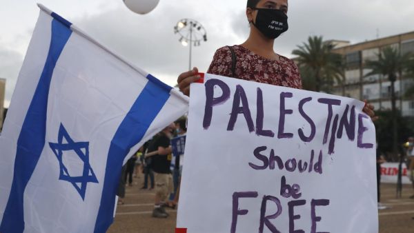 A protester, wearing a protective mask due to the COVID-19 pandemic, holds placards during a demonstration in Tel Aviv's Rabin Square to denounce Israel's plan to annex parts of the occupied West Bank, on June 23, 2020. Only a week before Prime Minister Benjamin Netanyahu intends to kick-start annexation plans in the occupied West Bank, Israel's premier is facing challenges at home and abroad. JACK GUEZ / AFP