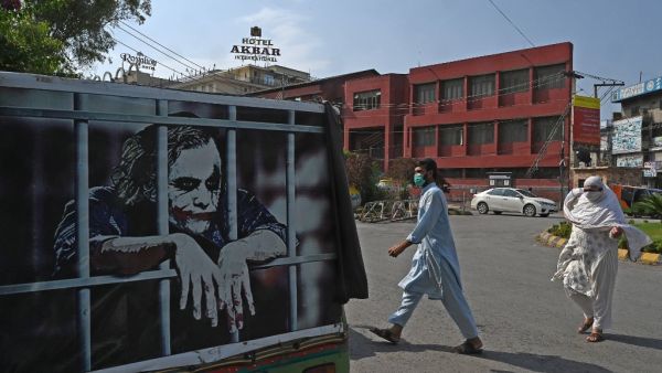 People wearing facemasks cross a street beside an auto-rickshaw with a graffiti depicting actor Heath Ledger (L) in his role as the Joker, in Rawalpindi on June 26, 2020.  Aamir QURESHI / AFP