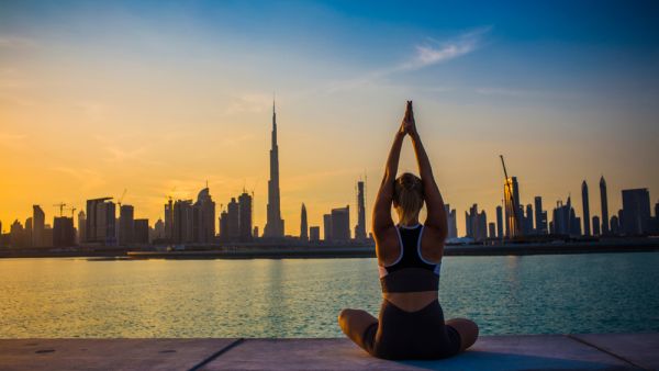 Young yogi woman doing sunset yoga with Dubai skyline view. (Shutterstock)