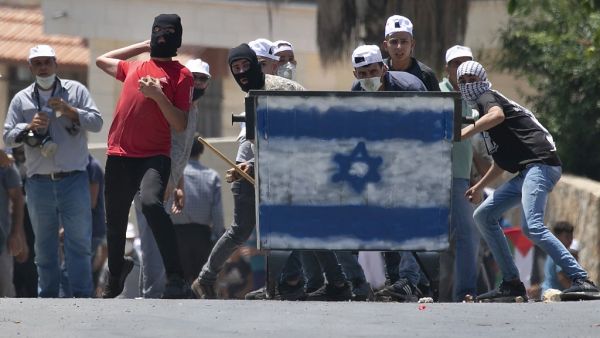 Palestinian protesters, standing behind a shield painted with the colours of the Israeli flag, hurl stones towards Israeli troops (unseen) during a demonstration in the village of Kfar Qaddum in the occupied West Bank against the Jewish state's plans to annex part of the Palestinian territory on July 3, 2020. Rival Palestinian factions Fatah and Hamas pledged the previous day a united campaign against Israel's prospective plans to annex territory in the occupied West Bank, in a rare joint press conference, 