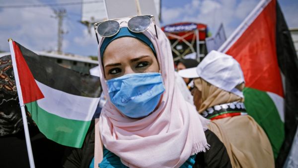 A Palestinian woman wearing a protective mask amid the COVID-19 pandemic lifts a national flag during a rally for supporters of the Fateh movement against Israel's West Bank annexation plans, in Beit Hanun in the north of the Gaza Strip, on July 6, 2020. MOHAMMED ABED / AFP