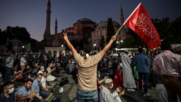 A man flashes the V for Victory hand sign and waves a flag outside the Hagia Sophia museum in Istanbul on July 10, 2020 as people gather to celebrate after a top Turkish court revoked the sixth-century Hagia Sophia's status as a museum, clearing the way for it to be turned back into a mosque. Ozan KOSE / AFP