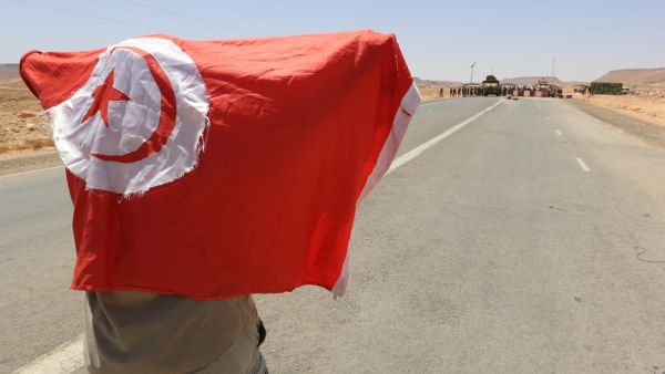 A man waves a national flag in front of Tunisian army soldiers gathered on July 12, 2020, at the border post with neighbouring Libya near the southern town of Dehiba, during a protest by Tunisians expressing their anger after the death earlier this week of a young man who according to demonstrators was killed by the military,  FATHI NASRI / AFP
