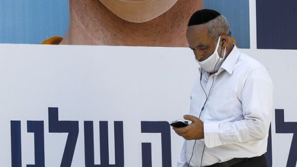 A mask-clad man browses his phone as he walks past a billboard showing other mask-clad faces and adequate social distance measures, raising awareness about COVID-19 coronavirus pandemic precautions, in the centre of the Israeli city of Ramat Gan, east of Tel Aviv, on July 17, 2020. Israel's government said it was imposing new restrictions to limit the spiraling spread of coronavirus in the hope of avoiding a general lockdown further along the line. It said that from 5:00pm local time (1400 GMT) on Friday un