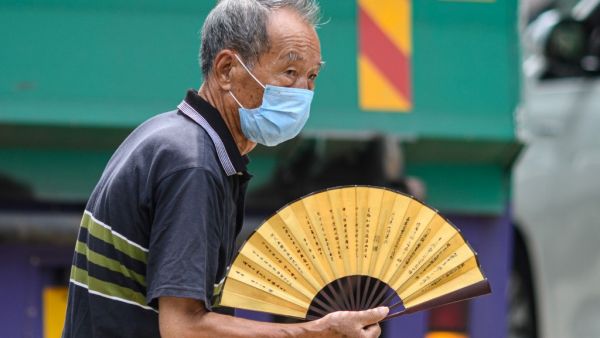 A man uses a traditional Chinese fan as he walks across a main road in Hong Kong on July 20, 2020. ANTHONY WALLACE / AFP