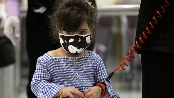 A girl wearing a protective mask and a child safety leash waits with members of her family to board a flight at the departure hall of Baghdad international airport following its reopening on July 23, 2020, after a closure forced by the coronavirus pandemic restrictions aimed at preventing the spread of the deadly COVID-19 illness in Iraq. AHMAD AL-RUBAYE / AFP