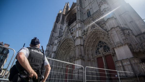 In this file photo taken on July 20, 2020 a police officer stands in front of the partially burnt facade of the Saint-Pierre-et-Saint-Paul Cathedral in Nantes, western France. Loic VENANCE / AFP