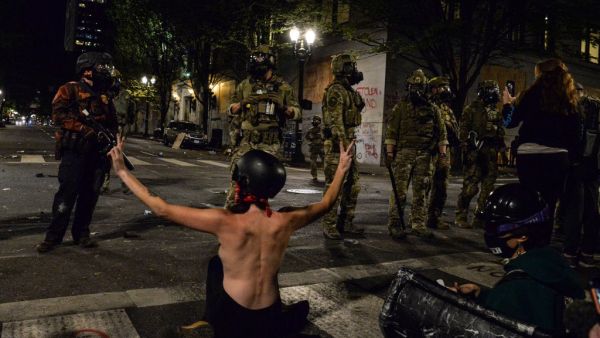 A topless protestor (C) gestures in front of federal police personnel in Portland, Oregon early July 26, 2020, as protests continue across the United States following the death in Minneapolis of unarmed African-American George Floyd. (AFP/File)