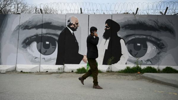 A man wearing a facemask against coronavirus walks past a wall painted with images of US Special Representative for Afghanistan Reconciliation Zalmay Khalilzad and Taliban co-founder Mullah Abdul Ghani Baradar, in Kabu'. AFP | WAKIL KOHSAR