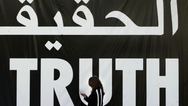 A file photo taken on April 5, 2005 shows a Lebanese woman using her mobile as she walks past a giant banner reading "truth" in Arabic and English in the Lebanese capital Beirut. A massive bomb tore through Hariri's armoured convoy as he drove home for lunch on Valentine's Day 2005, killing him and 21 other people including seven of his bodyguards, as well as wounding 226 others. A UN-backed court is to deliver its judgement on August 7, 2020, on four suspected Hezbollah members tried in absentia for former
