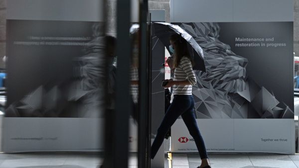 A woman walks past an HSBC lion graphic outside the local headquarters of the bank in Hong Kong on August 3, 2020. HSBC said on August 3, 2020 its first half post-tax profits for 2020 plunged 69 percent on year as the Asia-focused banking giant was hammered by the coronavirus and spiralling China-US tensions. Anthony WALLACE / AFP