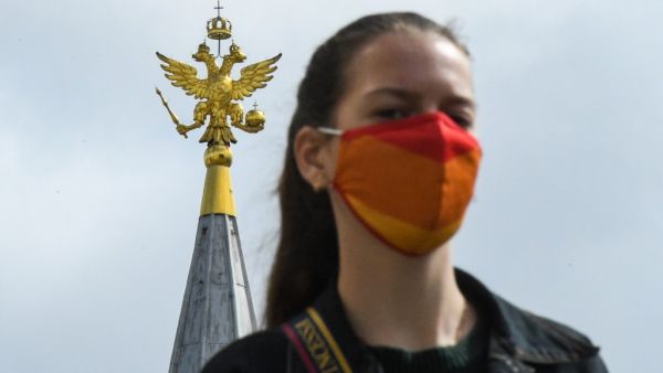 A woman wearing a face mask to protect against the coronavirus disease walks in front of a two-headed eagle, the national symbol of Russia, at the top a building on Red Square in downtown Moscow on August 12, 2020. Russia claimed on August 11 it has developed the world's first vaccine offering "sustainable immunity" against the coronavirus, despite mounting scepticism about its effectiveness as fears grow over a second wave of infections across the globe. Kirill KUDRYAVTSEV / AFP