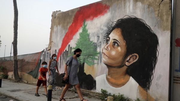 Mask-clad pedestrians walk past a mural painting on September 4, 2020, depicting a young Lebanese girl who suffered a face injury in the August 4 massive blast at the nearby seaport, one month after the disaster that left scores of people dead or injured and ravaged swaths of the capital Beirut. JOSEPH EID / AFP