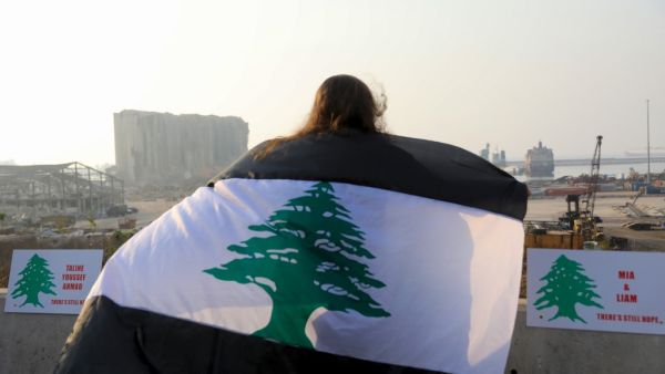 A woman, draped in a black-striped Lebanese flag, looks at the site of the massive explosion at Beirut's port area, during a demonstration to mark one month since the cataclysmic August 4 explosion that killed 191 people, in the Lebanese capital Beirut on September 4, 2020. The explosion piled on new misery for Lebanese already reeling from the coronavirus pandemic and the country's worst economic crisis in decades. As well as killing more than 190 people, the explosion injured at least 6,500 and left 300,0