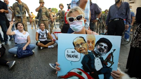 A Lebanese anti government protester holds a placard with a cartoon of (L-R) President Michel Aoun, Parliament Speaker Nabih Berri and head of the Shiite movement Hezbollah Hassan Nasrallah sitting atop a national flag. ANWAR AMRO / AFP