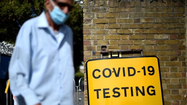 A man wearing a face covering due to the COVID-19 pandemic, waks past a sign outside a novel coronavirus walk-in testing centre in East Ham in east London, on September 17, 2020. British Prime Minister Boris Johnson said Thursday he could close pubs earlier to "stop the second hump" of coronavirus cases, comparing the country's trajectory of resurgent transmission to a camel's profile. But the prime minister has faced stinging criticism this week over the failure to achieve the "world-beating" testing and t