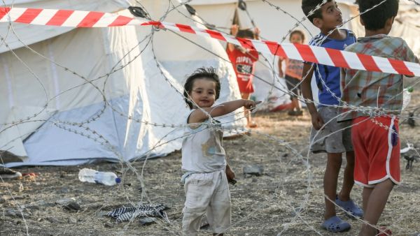 Youngsters of migrant families stand behind barbwire at a quarantine area in the new temporary camp near Mytilene on the Greek island of Lesbos, as more than 200 people were diagnosed with COVID-19, on September 19, 2020.  MANOLIS LAGOUTARIS / AFP