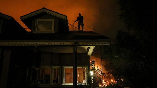Michael Kunch uses a garden hose to water down his roof as a protective measure as the Bobcat Fire burns down a nearby hillside on September 15, 2020 in Monrovia, California. MARIO TAMA / GETTY IMAGES NORTH AMERICA / Getty Images via AFP