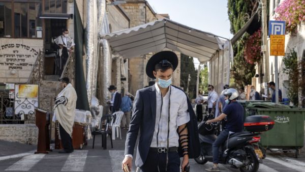 An Ultra-orthodox Jewish man clad in face mask and wearing Tefillin or phylacteries (small black leather box containing scrolls of parchment inscribed with verses from the Torah) walks past others praying outdoors in Jerusalem, during the second nationwide lockdown imposed by the government in a bid to stem the increase of COVID-19 coronavirus cases, on October 1, 2020. MENAHEM KAHANA / AFP
