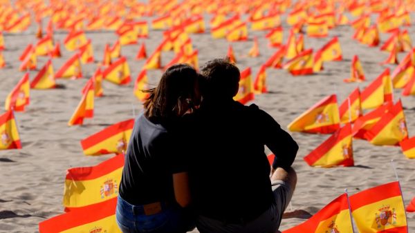 In this file photo taken on October 4, 2020 a couple sit next to thousands of Spanish flags, representing the Spanish victims of COVID-19, on Patacona beach in Valencia. Spain surpassed one million virus cases on October 21, 2020 according to health ministry figures. Jose Jordan / AFP