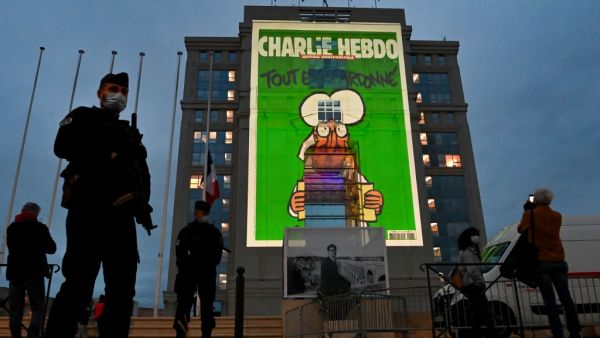 Police officers stand guard as cartoons of French satirical weekly newspaper Charlie Hebdo are projected onto the facade of the Hotel de Region in Montpellier, on October 21, 2020, during a national homage to French teacher Samuel Paty who was beheaded for showing cartoons of the Prophet Mohamed in his civics class. (AFP)