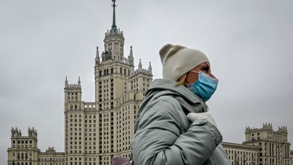 A woman wearing a face mask to protect against the coronavirus disease walks along a bridge near a Stalin-era skyscraper in central Moscow on October 22, 2020. Yuri KADOBNOV / AFP