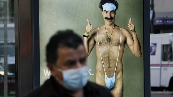 In this file photo taken on October 15, 2020, person wearing a mask walks past a bus stop ad on October 15, 2020, for the upcoming movie "Borat 2," featuring actor Sacha Baron Cohen, ahead of its release on October 23. US President Donald Trump said he has not been a fan of Sacha Baron Cohen, even before a clip from the British comedian's new Borat movie forced the US president's lawyer Rudy Giuliani into an awkward explanation. Asked about the clip, which shows Giuliani in a faked "interview" with an attra
