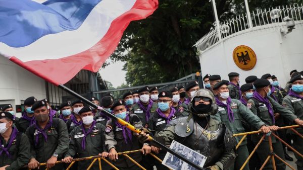 A royalist supporter waves a large Thai national flag in front of police standing guard during a rally outside the German embassy to show support for the Thai royal establishment in Bangkok on October 26, 2020. Jack TAYLOR / AFP