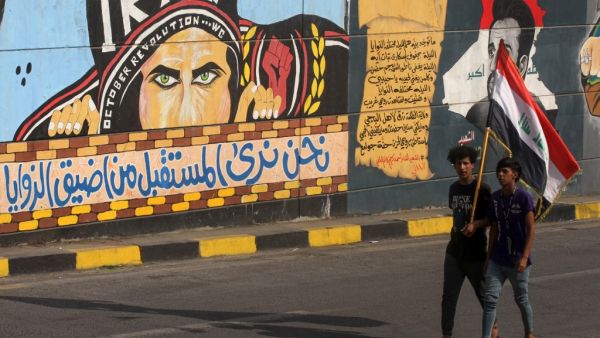 Iraqi youths carry a national flag as they walk past a mural painting in the capital Baghdad's Tahrir Square on October 28, 2020, during a cleanup operation by security forces allowing roads around the city centre, the scene of anti-government protests, to reopen. AHMAD AL-RUBAYE / AFP