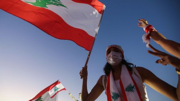A Lebanese protester lifts a national flag during a demonstration marking the one year anniversary of the beginning of a nationwide anti-government protest movement, in the capital Beirut on October 17, 2020. Hundreds marched in Lebanon's capital to mark the first anniversary of a non-sectarian protest movement that has rocked the political elite but has yet to achieve its goal of sweeping reform. ANWAR AMRO / AFP