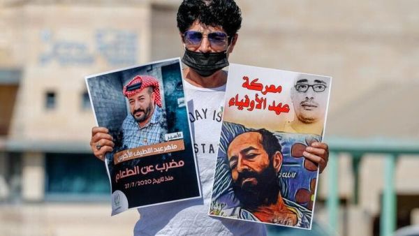 An Israeli left-wing activist lifts posters during a demonstration calling for the release of Palestinian administrative detainees, including Maher al-Akhras, (image L) who's health has deteriorated while on hunger strike, during a protest outside the Israeli run Ayalon prison in Ramle near the coastal city of Tel Aviv, on October 24, 2020. AHMAD GHARABLI / AFP