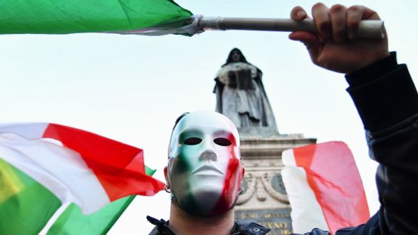 A protestor, wearing a mask in the colors of the Italian flag, holds a flag as he takes part in a protest rally against a new series of restrictions to stop a rise in Covid-19 cases, even as the government considers more stringent measures, in Rome on October 31, 2020. Alberto PIZZOLI / AFP