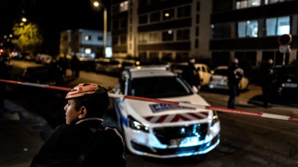 A boy wearing an Halloween mask looks away in foreground as French soldiers and Municipal Police officers stand behind a cordon-off area near the Orthodox Church where an attacker armed with a sawn-off shotgun wounded an Orthodox priest in a shooting before fleeing, on October 31, 2020 in Lyon, said a police source. JEFF PACHOUD / AFP