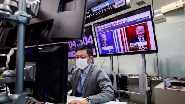 A currency trader works at his desk as a screen shows news updates on the US presidential election featuring portraits of US President Donald Trump (R) and Democratic Party candidate Joe Biden, at a foreign exchange trading company in Tokyo on November 5, 2020. Behrouz MEHRI / AFP