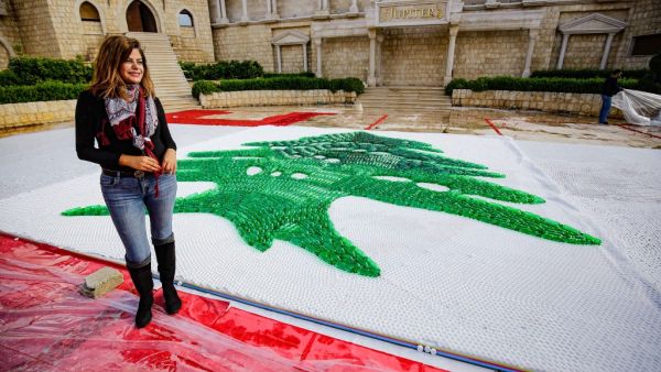 Caroline Chaptini, an environmental activist, poses next to a partially-completed 300-square-metre Lebanese national flag made up from plastic bottles, caps, and empty bullet cartridge set up by activists at an open-air restaurant and wedding venue in the town of Bnachii in northern Lebanon on November 21, 2020, a day ahead of the country's 77th independence day. Ibrahim Chalhoub / AFP