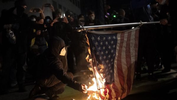 Black bloc protesters burn an American flag on November 4, 2020 in Portland, Oregon. Multiple protests, some peaceful and others violent, broke out in Portland as the presidential election remained undecided. Nathan Howard/Getty Images/AFP
