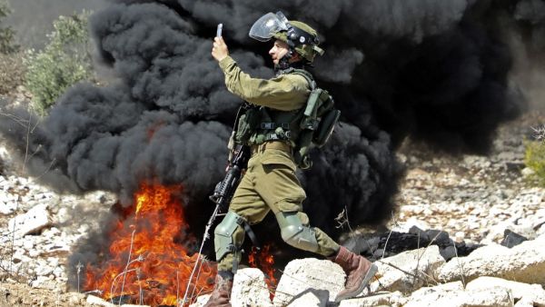 A member of the Israeli security forces takes a photograph with his telephone during clashes with Palestinian protesters after a weekly demonstration in the West Bank village of Kfar Qaddum, on October 23, 2020. JAAFAR ASHTIYEH / AFP
