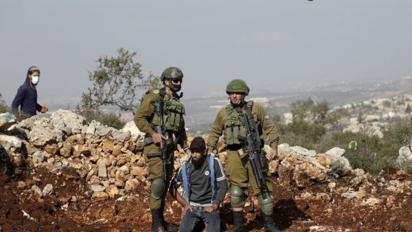 Israeli soldiers detain a Palestinian protester as an Israeli settler hurls rocks at Palestinians during a demonstration against the expansion of settlements in the occupied-West Bank town of Salfit, near the Israeli settlement of Ariel, on November 30, 2020. JAAFAR ASHTIYEH / AFP