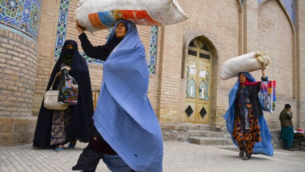 Burqa-clad women carry their belongings as they walk past the Jama Mosque in Herat on December 3, 2020. HOSHANG HASHIMI / AFP