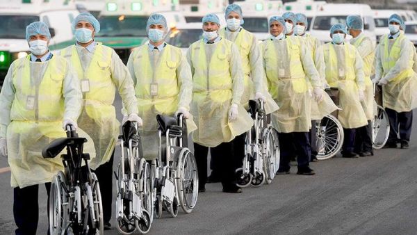 Ministry of Health workers, dressed in protective suits, wait on the runway at Kuwait International Airport to greet Kuwaitis returning from Frankfurt on 26 March 2020