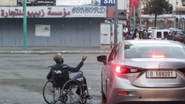 A wheelchair-bound beggar is seen next to a car stopping at a red light, in Lebanon's capital Beirut on January 16, 2021, despite a total lockdown due to the COVID-19 coronavirus pandemic. ANWAR AMRO / AFP