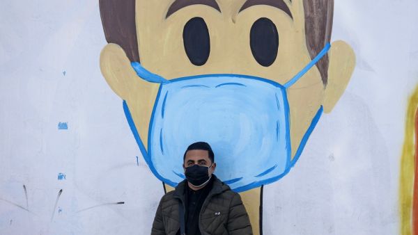 A Palestinian man sits in front of a coronavirus mural as part of the COVID-19 awareness campaign, in Khan Yunis in the southern Gaza Strip on January 20, 2021. SAID KHATIB / AFP