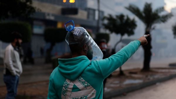 A Lebanese anti-government protester wearing a water bottle as a shield points during clashes with security forces in front of the Serail (headquarters of the Governorate), in the northern port city of Tripoli, following a demonstration to protest against the economic situation, on January 28, 2021. Tripoli was already one of Lebanon's poorest areas before the coronavirus pandemic piled new misery onto a chronic economic crisis. Many of its residents have been left without an income since Lebanon imposed a 